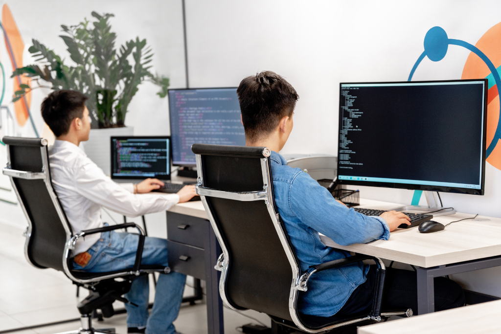 Two developers working side by side at their desks in an office
