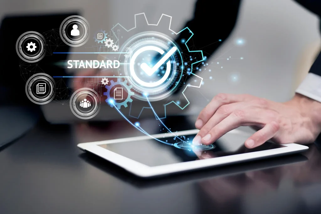 A hand using a tablet that displays digital standard icons and process gears